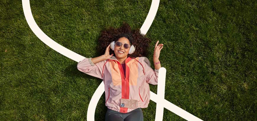 A person lies on grass listening to headphones, with white lines painted on the ground.