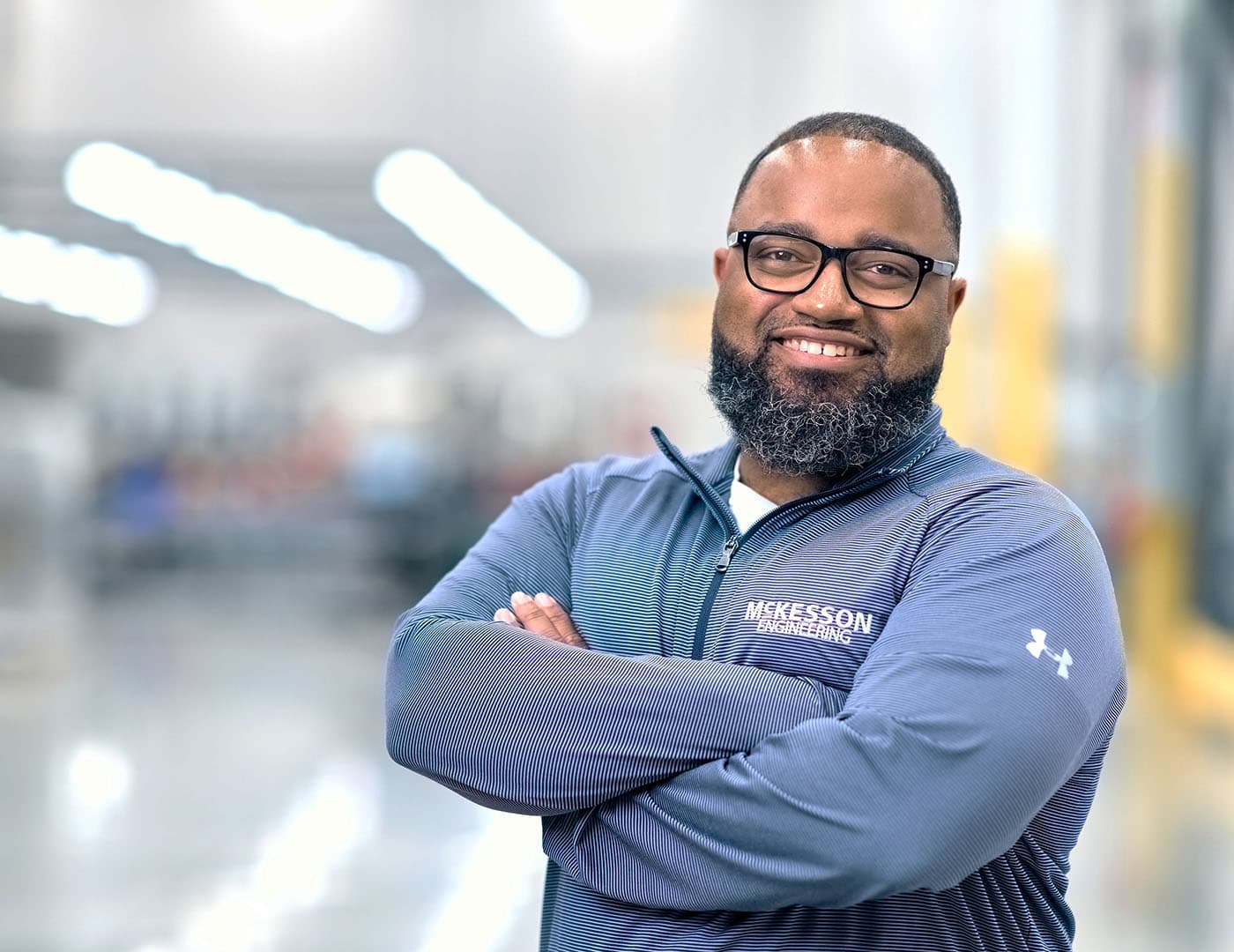 Person in a blue McKesson-branded jacket with arms crossed, standing in an industrial or warehouse setting.