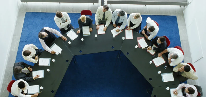 Aerial view of business meeting around a U-shaped table with papers and coffee cups.