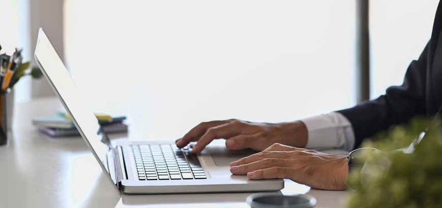 A person in a suit typing on a laptop at a bright, modern desk.