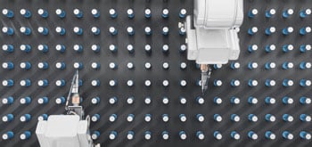 Robotic arms sorting small white and blue bottles on a conveyor grid.