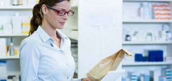 A person in a pharmacy holding a paper bag and a piece of paper.