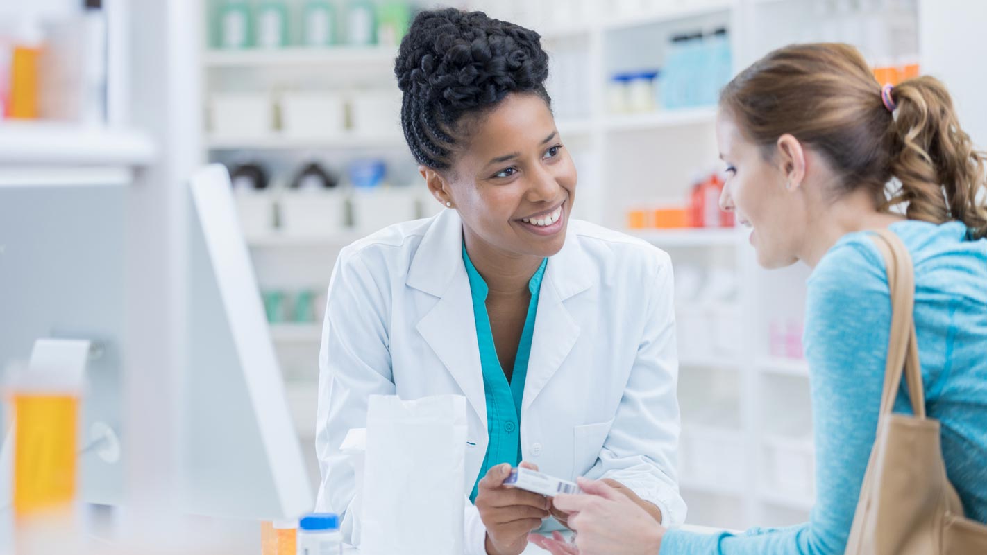 A pharmacist in a white coat assists a customer in a pharmacy.