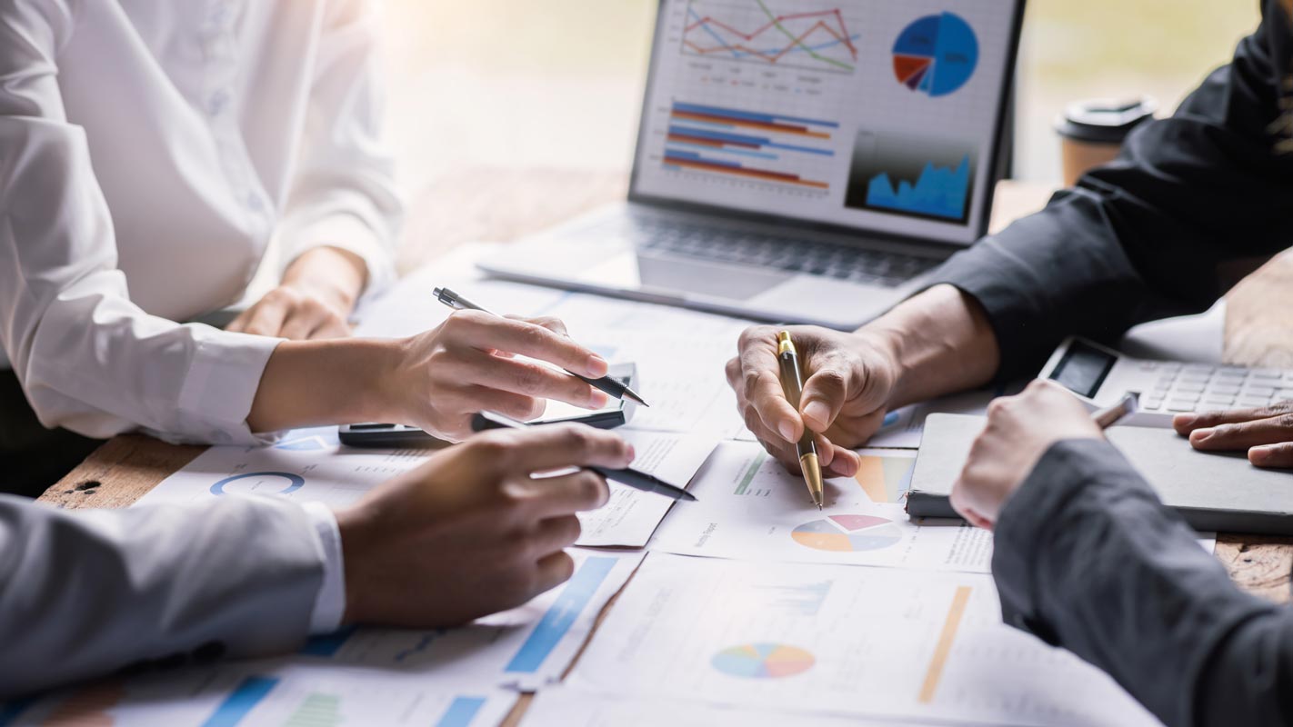 A group of people collaborates on documents with charts and graphs spread on a table.