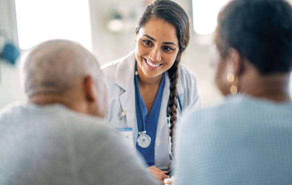 A doctor with a stethoscope around the neck speaks to two patients in an office.